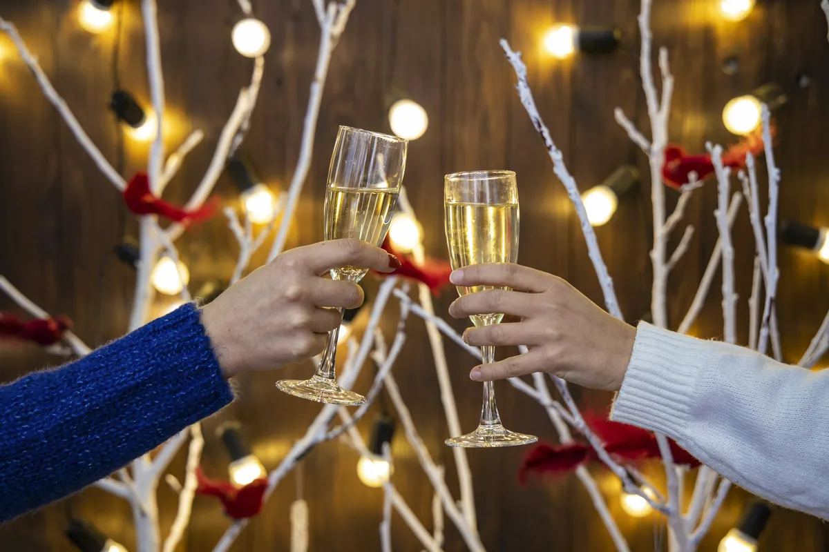 Two glasses of sparkling wine raised in a toast under holiday lights
