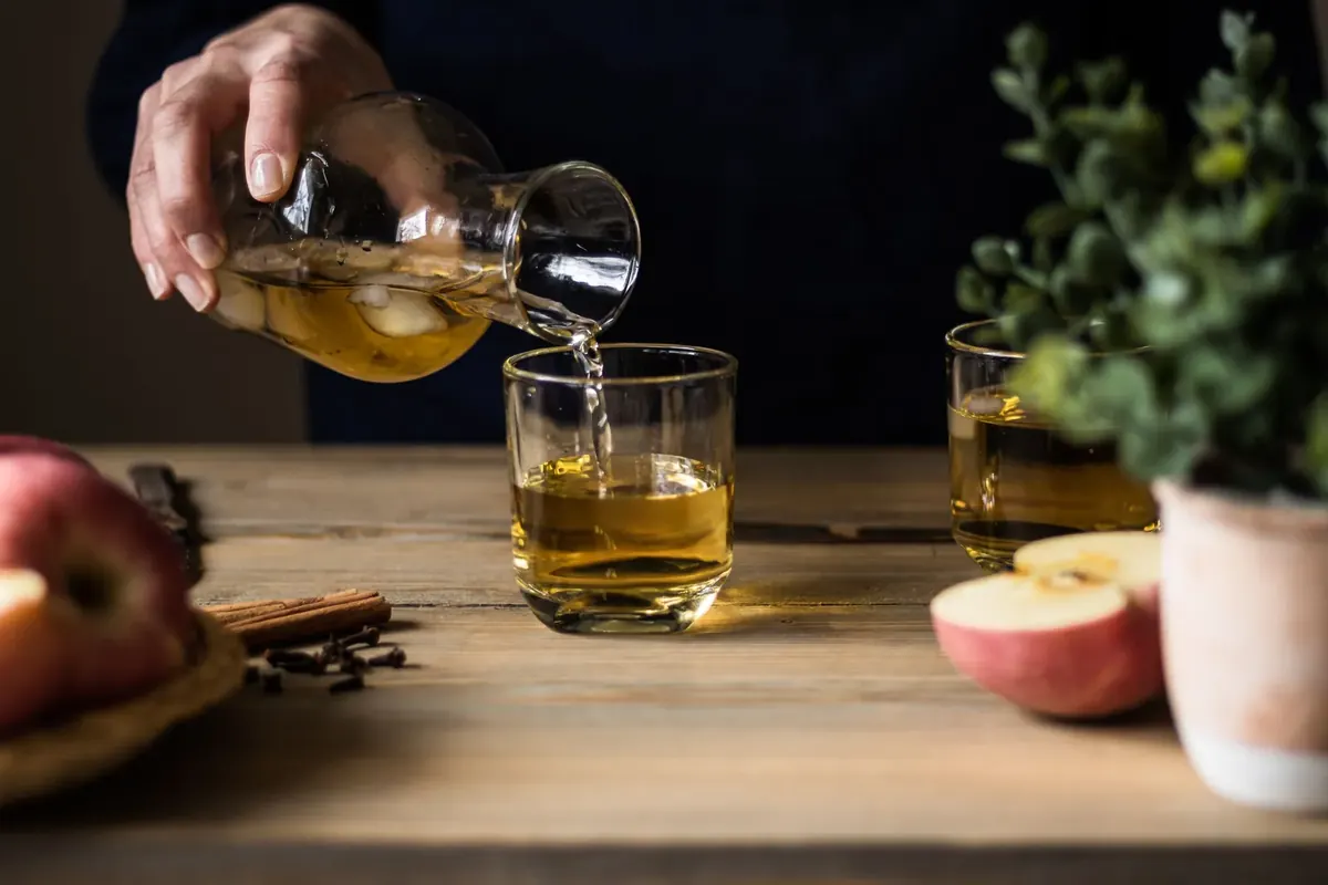 Apple cider being poured into glasses on a wooden table