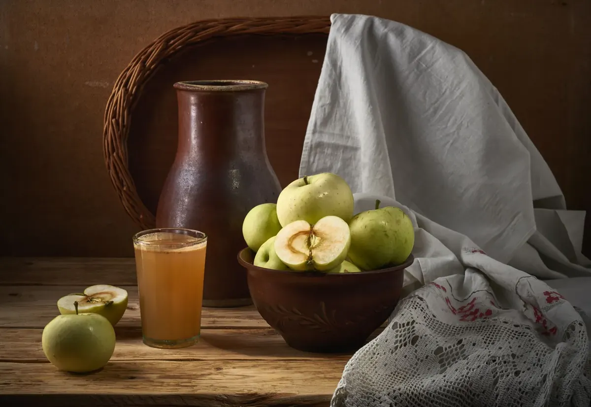 Glass of cider beside a jug and a bowl of green apples