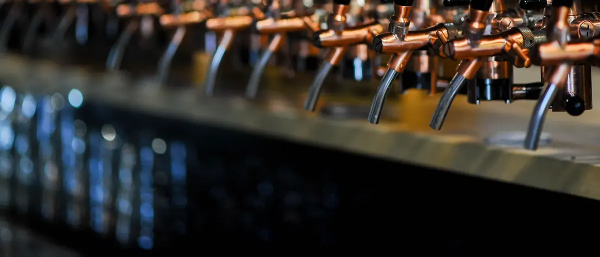 Row of copper beer taps along a taproom bar